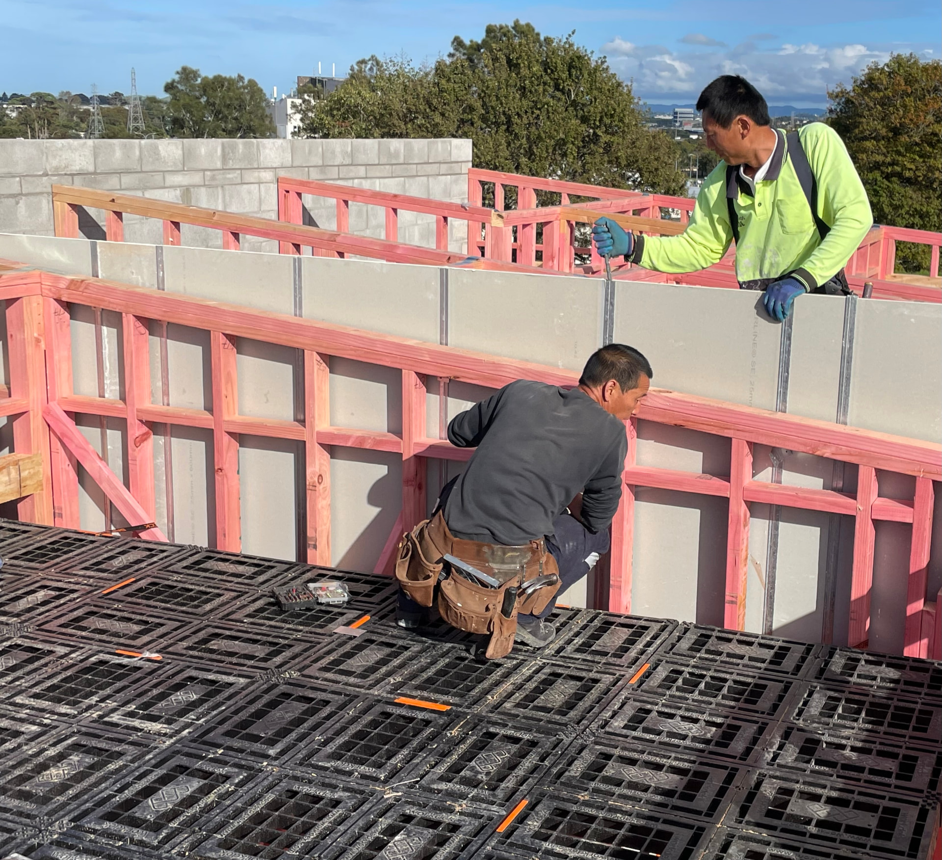 Two builders working at the edge of a Workdek platform next to a concrete party wall