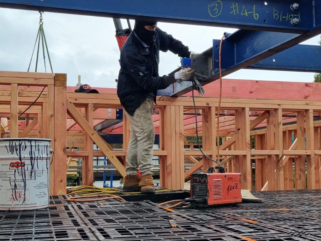 Builder welding a steel beam while standing on a Workdek mid-floor platform