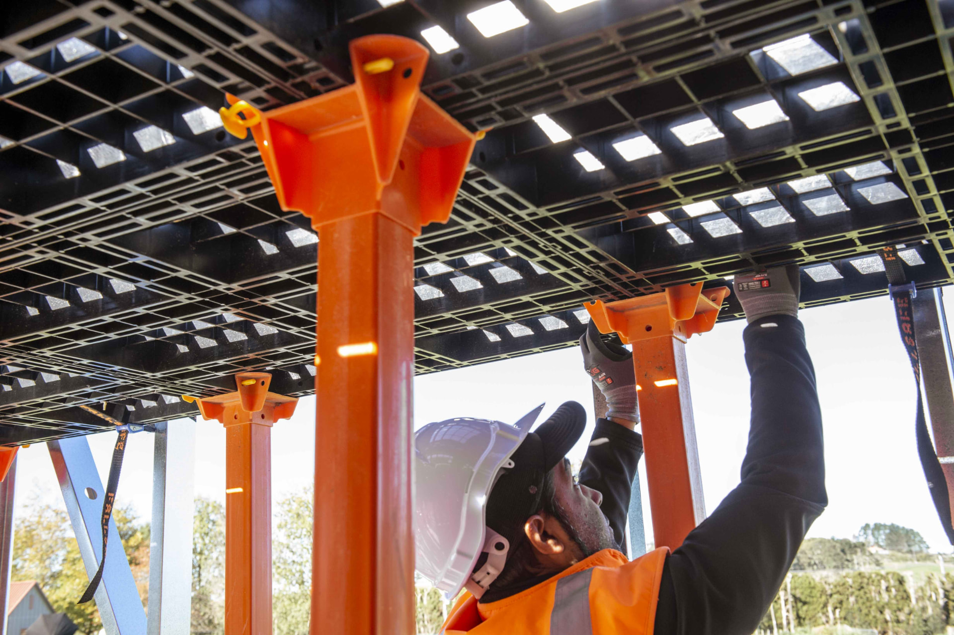 Installer locking a Workdek panel into an orange cradle on top of a leg, seen from below