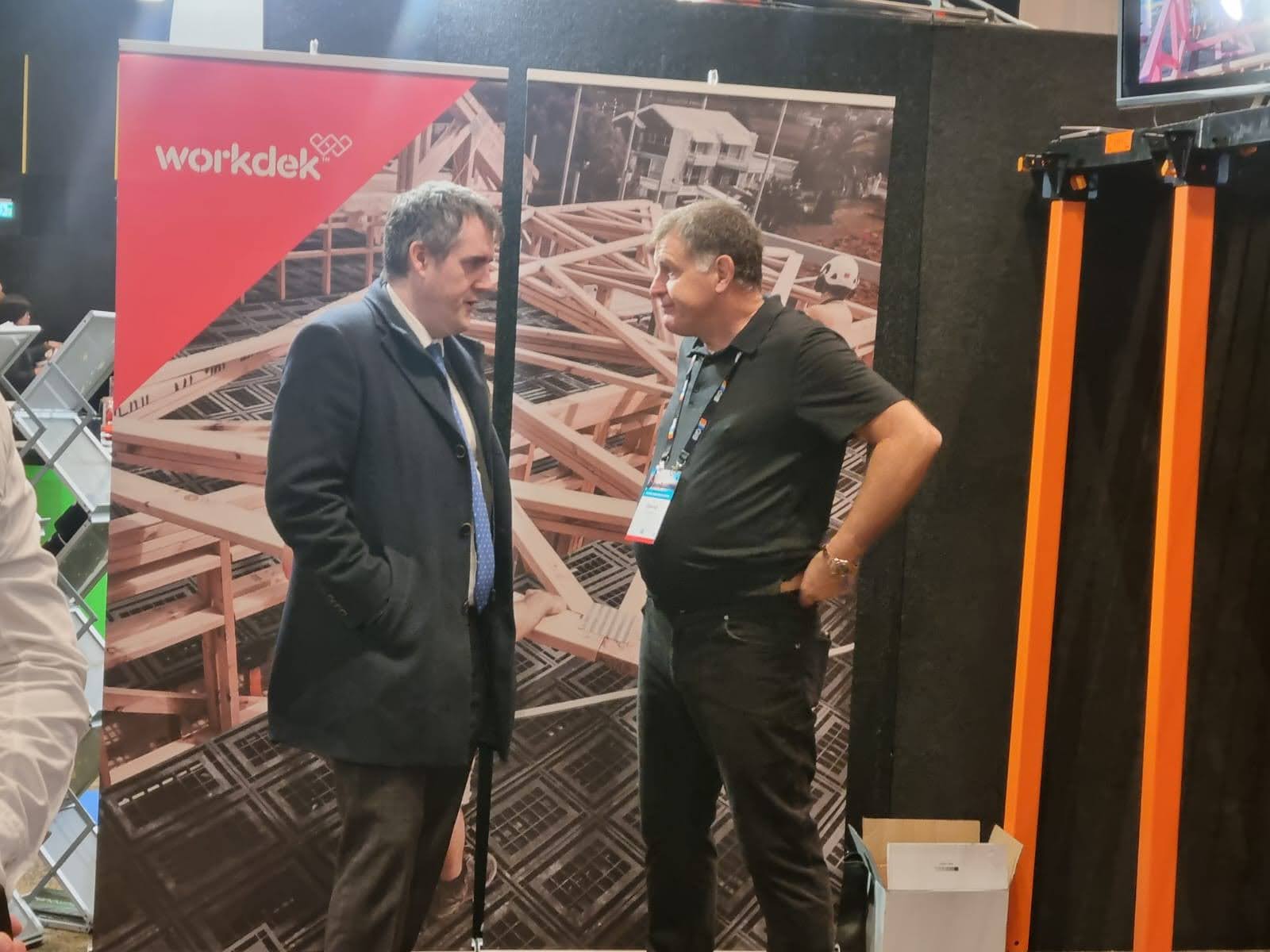Two people talking in front of a Workdek display stand at an industry event