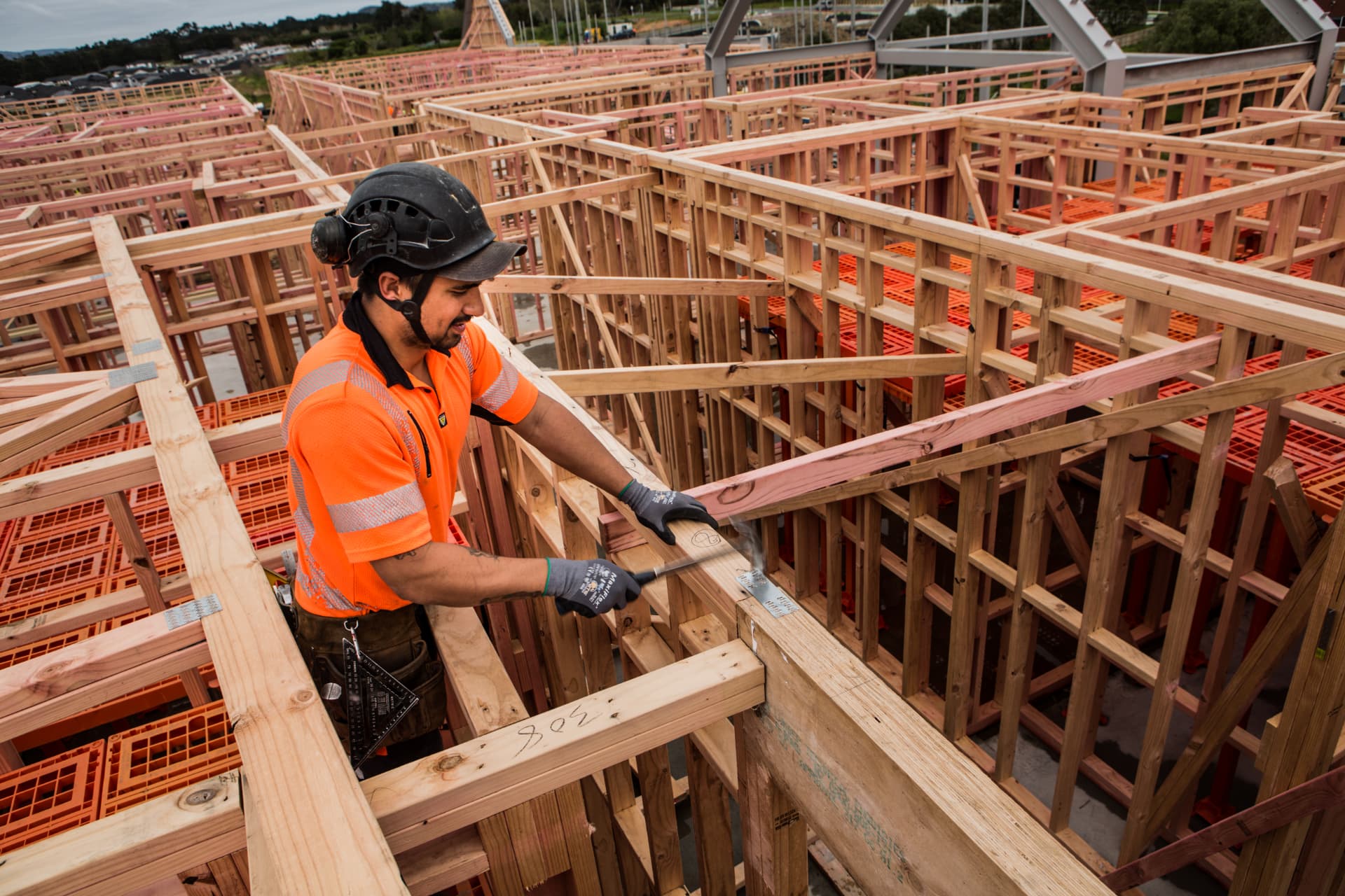 Builder fixing timber at top plate level with orange Workdek panels covering the floor below