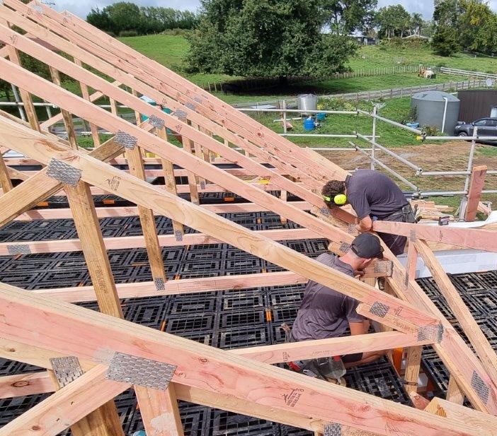 Two builders fixing rafters with a black Workdek deck covering the floor below them