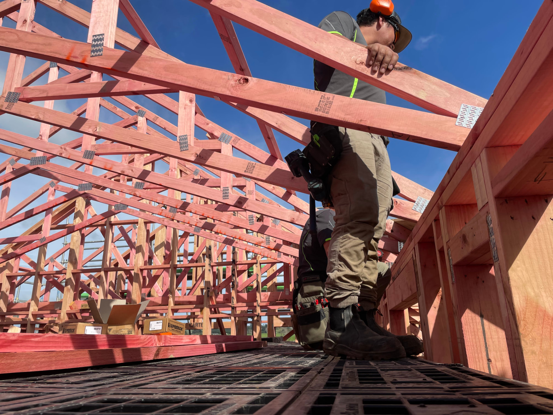 Builder carrying timber across a platform beneath a framed roof